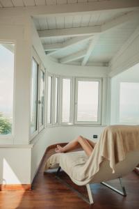 a woman laying on a bed in a room with windows at Al Mirador Resort in Selva di Fasano