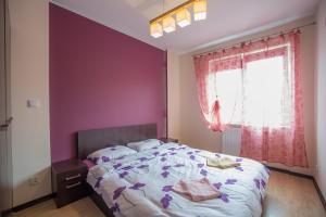 a bedroom with a bed with purple walls and a window at Słoneczny Apartament in Giżycko