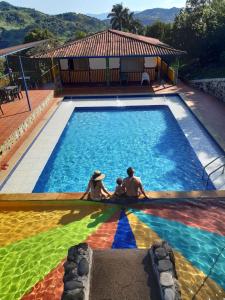 una familia sentada en una piscina con una bandera arco iris en Finca Hotel Guayacundo, en Vergara