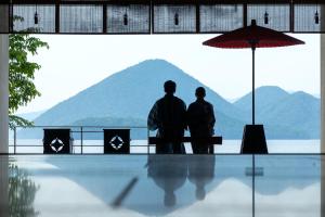 two people standing under an umbrella in front of a mountain at Toya Kohan Tei in Lake Toya