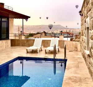 a pool with two chairs and hot air balloons in the sky at Balloon Cave Hotel in Göreme