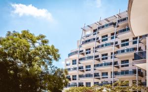 a white apartment building with trees in front of it at Kfar Maccabiah Business & Sport Hotel in Ramat Gan