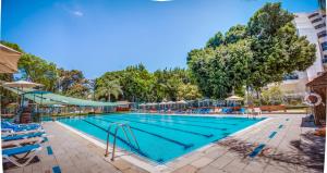 a large swimming pool with blue chairs and trees at Kfar Maccabiah Business & Sport Hotel in Ramat Gan