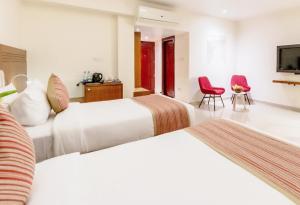 2 Betten in einem Hotelzimmer mit 2 roten Stühlen in der Unterkunft DVG Socials Retreat in Davanagere