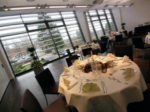 a dining room with white tables and chairs and large windows at Hotel am See in Salzgitter