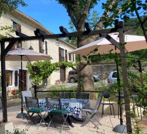 un patio con mesa, sillas y sombrillas en Les Deux Chevaux Chambres d’Hôtes, en Rouvenac