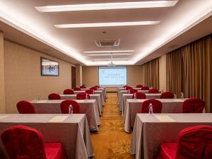 una sala de conferencias con mesas, sillas rojas y una pantalla en Vienna Hotel Guangzhou Panyu NanCun, en Guangzhou