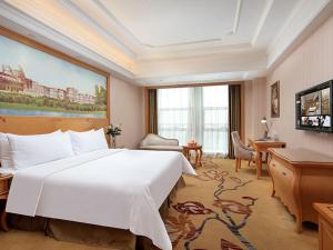ein Hotelzimmer mit einem großen weißen Bett und einem Schreibtisch in der Unterkunft Vienna International Hotel Jiujiang Shili Street in Jiujiang
