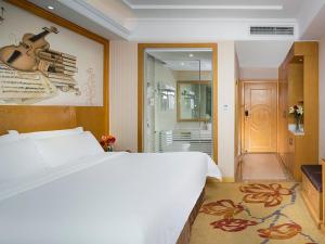 a bedroom with a large white bed and a guitar on the wall at Vienna Classic Hotel Ganzhou Meilin in Ganzhou