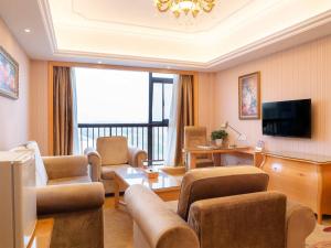 Vienna International Hotel Shanghai Pudong New District Dishui Lake Univeristy City في Nianbalian: غرفة معيشة مع أريكة وكراسي وتلفزيون