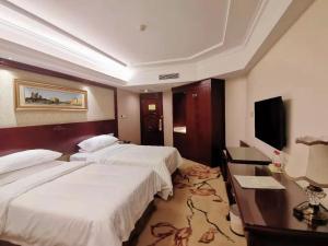 een hotelkamer met 2 bedden, een bureau en een televisie bij Vienna Hotel Changnan in Nanchang County