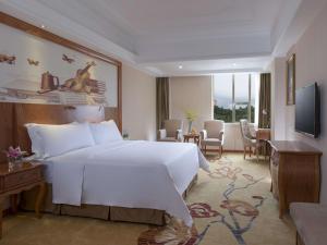 Vienna International Hotel Shenzhen Caopu Jindaotian في شنجن: غرفة نوم بسرير ابيض كبير وغرفة معيشة