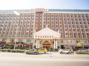 un grand bâtiment avec des voitures garées devant lui dans l'établissement Vienna International Hotel Shanghai Pudong Xiupu Road, à Shanghai