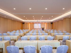 Vienna Hotel Yangjiang Jiangcheng District في يانغجيانغ: قاعة اجتماعات بطاولات بيضاء وكراسي وشاشة