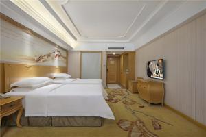 a bedroom with a large white bed and a television at Vienna Hotel Zhengzhou Zhongyuan Futa in Zhengzhou