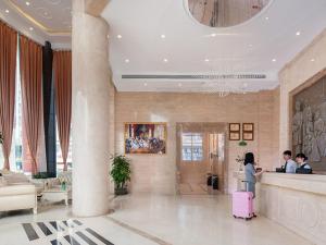 a woman with a pink suitcase in a hotel lobby at Vienna Hotel Dongguan Hou Avenue Jinzuo in Hetian