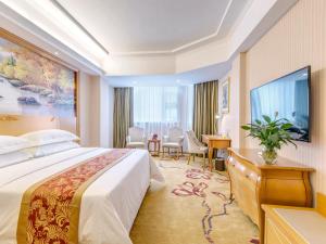 桂林市にあるVienna Hotel Guilin AIrport Road Rongshanのベッド、テーブル、椅子が備わるホテルルームです。