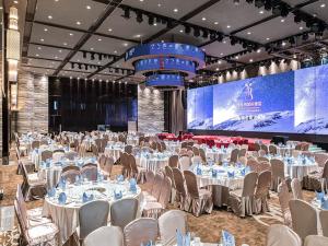 a banquet hall with white tables and chairs and a screen at Vienna International Hotel Foshan The World of Flowers in Shunde