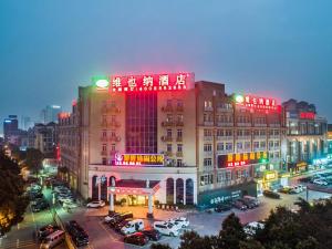 Vienna Hotel Shiqiao Metro Station في قوانغتشو: مبنى كبير به لافتات نيون في موقف للسيارات