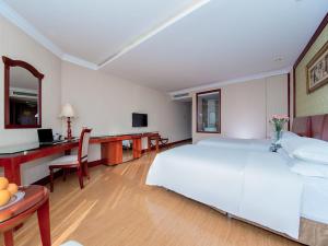 a bedroom with a large white bed and a desk at Vienna International Hotel Xiangyang Railway Station in Xiangyang