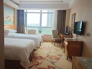 a hotel room with two beds and a desk and a television at Vienna Hotel Liaocheng University in Liaocheng