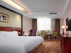 Habitación de hotel con cama, mesa y sillas en Vienna International Hotel Huizhou South Railway Station, en Huizhou