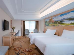 Vienna Hotel Tongcheng Tongkang Road في Tongcheng: غرفة فندقية بسريرين ولوحة على الحائط