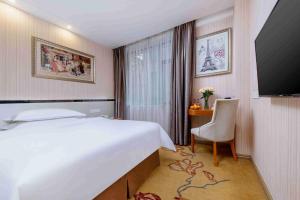 a hotel room with a bed and a desk and a television at Vienna Hotel Shenzhen Bantian Gangtou in Tiantangwei