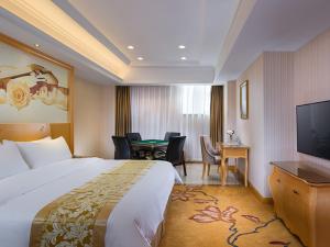 Cette chambre comprend un lit, un bureau et une télévision. dans l'établissement Vienna Hotel Guangdong Gaozhou City East Passenger Depot, à Dongguan