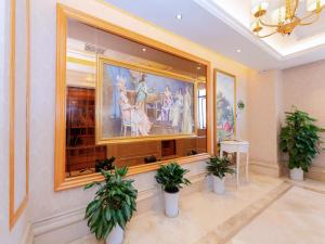 een kamer met een groot schilderij aan een muur met twee potplanten bij Vienna Hotel Shenzhen Longgang Ainan Road in Longgang