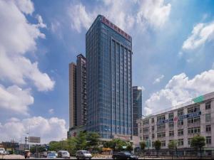 un edificio de cristal alto con coches estacionados frente a él en Vienna Hotel Shenzhen Xiashuijing Subway Station, en Shenzhen