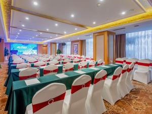 einen großen Bankettsaal mit einem grünen Tisch und weißen Stühlen in der Unterkunft Vienna Hotel (Mulian West Road Shop, Changsha) in Changsha