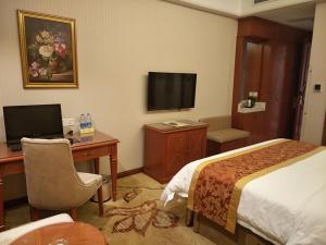 Cette chambre comprend un lit, un bureau et une télévision. dans l'établissement Vienna Classic Hotel Kongtong Avenue, à Pingliang