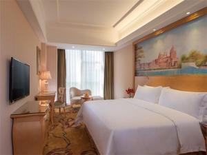 a hotel room with a large white bed and a television at Vienna International Hotel Guangzhou Jiaokou Subway Station in Nanhai