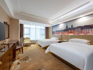 a hotel room with two beds and a large painting on the wall at Vienna Hotel Shenzhen Songgang Shajiang Road in Bao'an