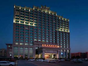 a large hotel building with cars parked in a parking lot at Vienna International Hotel Guangdong Zhongshanbei Station in Zhongshan