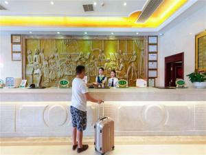 a man standing in front of a counter with a suitcase at Vienna Hotel Heyuan Hongxing Road in Heyuan
