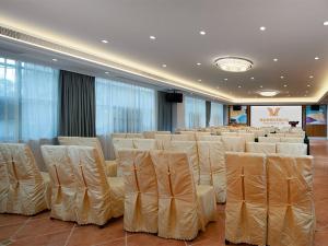una sala de conferencias con sillas blancas y un escenario en Vienna Hotel Chaozhou Plaza, en Chaozhou