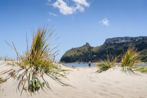 uma pessoa a caminhar numa praia de areia com relva em Arcobaleno Suites em Cagliari