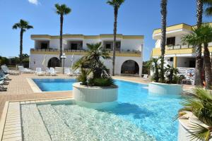 a swimming pool with palm trees in front of a building at Residence Club Costa D'Oriente in Torre dell'Orso