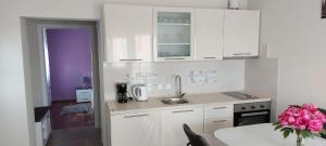 a kitchen with white cabinets and a table with pink flowers at Apartmani Katarina in Zadar