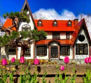 ein Haus mit orangefarbenem Dach und rosa Blumen in der Unterkunft Panketo Lodge & Yoga Studio in Hakuba