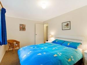 a bedroom with a blue bed and a chair at 37 Coastal Court Bush Retreat By the Sea in Dalmeny