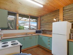 Una cocina con gabinetes azules y un refrigerador blanco. en 98 Ocean Parade Rustic Log Cabin, en Dalmeny 8 fotos más