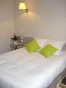 a white bed with two green pillows on it at Hotel-Restaurant Du Lac in Joue-les-Tours