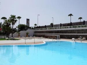a large blue swimming pool with chairs and palm trees at Lighthouse Friendly Holiday Home in Playa del Ingles