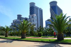 a person standing in a park with palm trees and buildings at Orbi Towers Rooms in Batumi