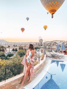 a woman standing next to a swimming pool with hot air balloons at Cappadocia Caves Hotel in Goreme