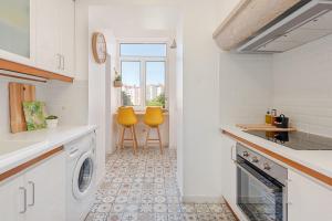 uma cozinha com uma máquina de lavar e secar roupa e 2 cadeiras amarelas em The Local Guest House Lisbon em Lisboa