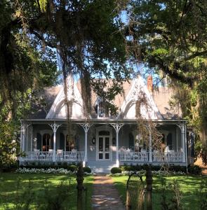 a white house with a porch and trees at St. Francisville Inn in Saint Francisville